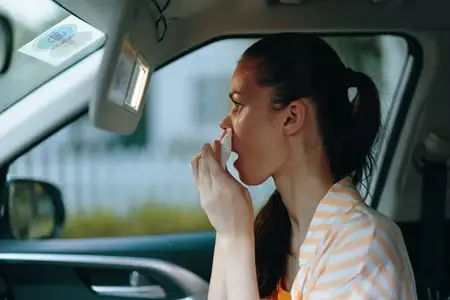 Женщина, сидя в машине, тщательно наносит макияж