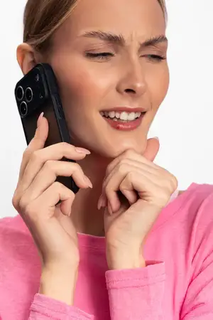 Крупный план женщины в розовом топе, прижимающей смартфон к уху, с закрытыми глазами, демонстрирующей задумчивое настроение