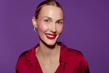 Счастливая женщина с глянцевыми красными губами и гладкой кожей позирует в красной рубашке и серьгах-кольцах