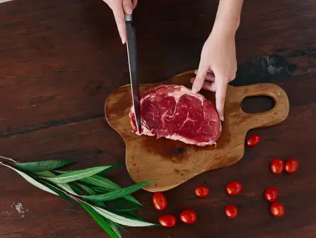 Женщина с ножом в руке нарезает свежее мясо стейка для жарки на кухне