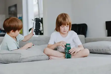 Сосредоточенный мальчик играет с зеленой игрушечной машинкой, а его младший брат возится с другой машинкой рядом