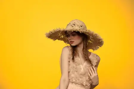 Женщина в соломенной шляпе, держащая её в руках, на жёлтом фоне, эмоции, обрезанный вид, крупный план