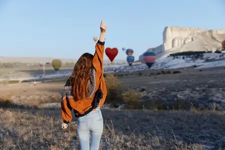 Женщина празднует свободу на залитом солнцем поле, а на заднем плане виден воздушный шар