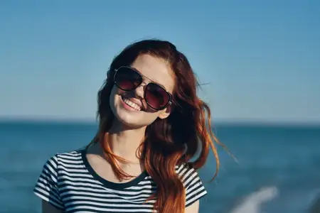 Рыжеволосая женщина-модель в футболке и солнцезащитных очках на фоне моря