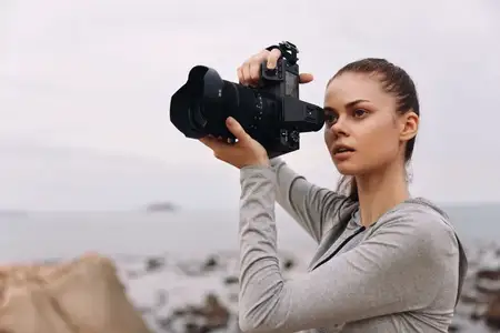 Молодой фотограф женского пола в сером спортивном топе сосредоточена на своей камере, запечатлевая красоту природы вдоль скалистой береговой линии