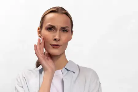 Блондинка со светлой кожей нежно касается лица, выражая замешательство или озабоченность