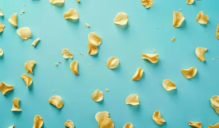 Красочная композиция из золотистых картофельных чипсов на бирюзовой поверхности усиливает визуальную привлекательность и располагает к моментам перекуса