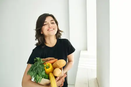 Весёлая женщина с пакетом продуктов делает домашнюю работу, связанную со здоровой едой