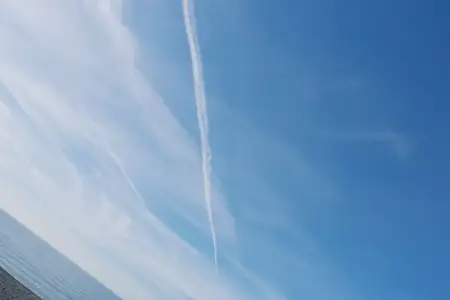 Чистое голубое небо с длинным инверсионным следом над водой