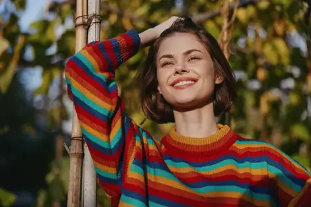 Женщина улыбается в цветном полосатом свитере на улице, наклонившись и глядя вверх, расслабленная поза