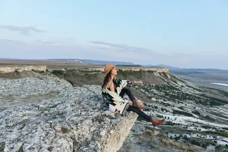 Безмятежная женщина сидит на краю утеса, глядя на величественную долину и горы