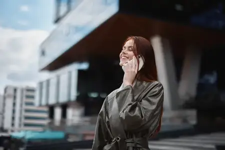 Женщина-бизнесмен разговаривает по телефону и улыбается, показывая зубы, на фоне городских зданий