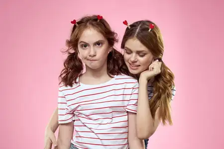 Счастливые сёстры веселятся на розовом фоне, на их головах — заколки-прищепки в форме сердечек