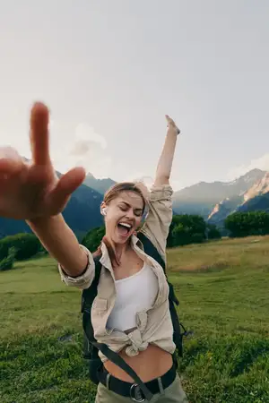 Непринуждённый жизненный снимок улыбающейся женщины, наслаждающейся природой во время прогулки на открытом воздухе, передающий энтузиазм и энергию похода в живописном пейзаже с ясным небом и зелёной…