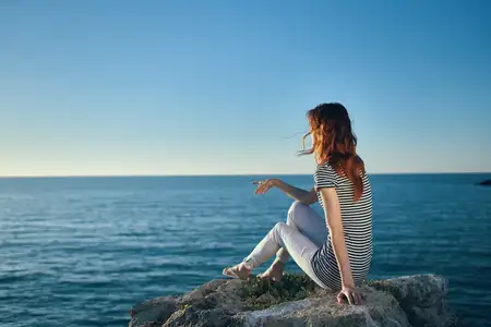 Красивая женщина на отдыхе в горах у моря, жестикулирующая руками на закате