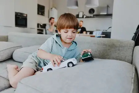 Радостный мальчик увлеченно играет с игрушечными машинками на мягком диване в стильной современной гостиной