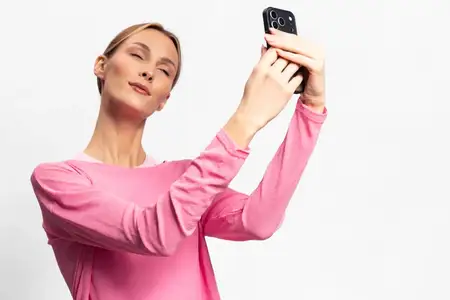 Женщина в розовом топе держит смартфон и делает селфи, изолированная на белом фоне