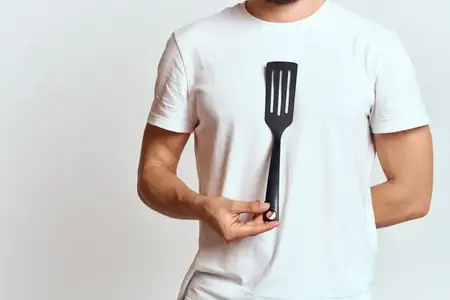 Мужчина с лопаткой для приготовления пищи, белая футболка, кадрированный вид, светлый фон