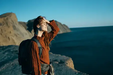 Симпатичная женщина в свитере с рюкзаком у моря на природе