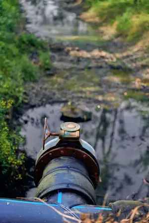 Труба и задвижка у дренажного выпуска, сбрасывающие воду в загрязненный ручей