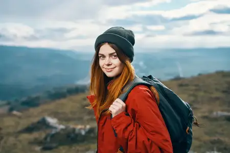 Портрет путешественника в красной куртке и шляпе, с рюкзаком на свежем воздухе в горах
