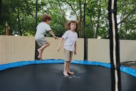 Двое энергичных мальчиков веселятся на батуте, прыгая и смеясь под ярким солнцем