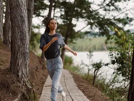 Энергичная бегунья тренируется на природе, одетая в удобную спортивную одежду, в окружении деревьев и живописного вида на спокойное озеро