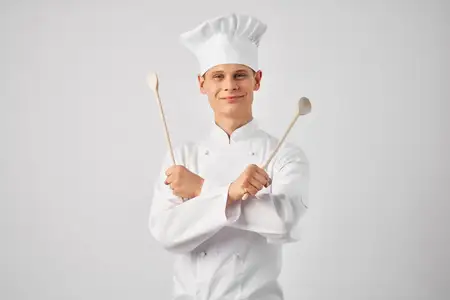 Мужчина в форме шеф-повара на кухне с кухонной утварью, передающий эмоции в ресторане