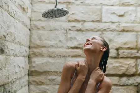 Счастливая женщина стоит под уличным душем, вода льётся на неё