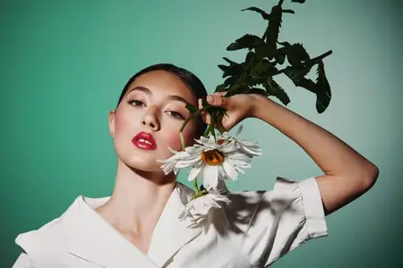 Молодая женщина в белой блузе позирует, держа крупные белые цветы маргаритки с выступающими оранжевыми серединками