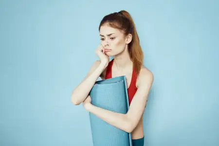 Спортивная женщина в красном топе на лямках занимается на коврике для фитнеса на синем фоне