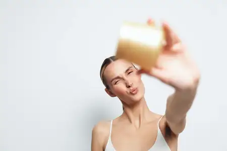 Улыбающаяся женщина с гладкой кожей демонстрирует баночку с косметическим кремом