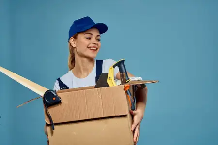 Работающая женщина в форме с коробкой в руках, инструменты, погрузка, служба доставки на голубом фоне