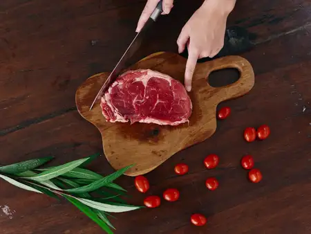 Женщина с ножом в руке нарезает свежее мясо для стейка, предназначенное для запекания на кухне