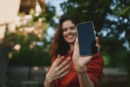 Яркая уличная сцена: улыбающаяся женщина делает селфи на смартфон, демонстрируя расслабленную моду и повседневную уверенность в залитом солнцем городском парке