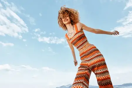 Счастливая улыбающаяся женщина танцует на пляже с рюкзаком, ощущая свободу хиппи-образа жизни
