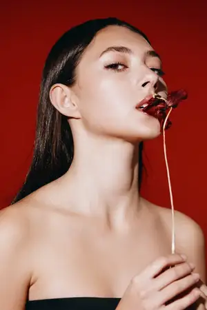 Симпатичная молодая женщина с алыми губами наслаждается вкусным леденцом на палочке на белом фоне