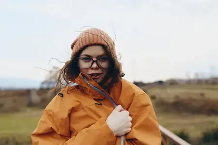 Женщина в зимней уличной куртке, очках и шапке-бини на открытом воздухе