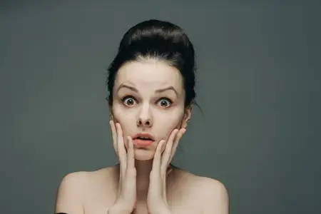 Испуганное женское лицо с обнажёнными плечами, причёска на сером фоне, модель