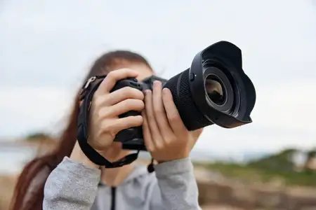 Молодая женщина с увлечением занимается фотографией на открытом воздухе, используя свою зеркальную камеру