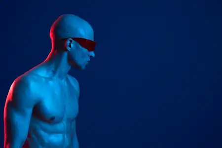 Это поразительное изображение запечатлело мускулистого мужчину в солнцезащитных очках на синем фоне, вызывая чувство современности и смелости