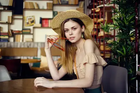 Симпатичная женщина в шляпе сидит за столом с книгами на заднем плане, крупный план