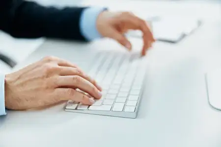 Руки лежат на клавиатуре настольного компьютера во время работы в офисе