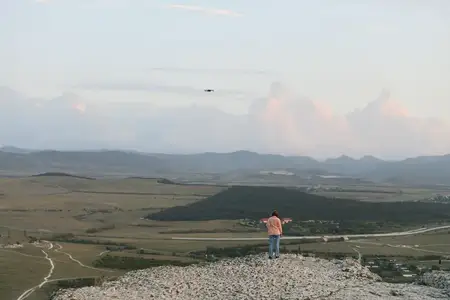 Человек стоит на вершине горы, в небе парит воздушный змей