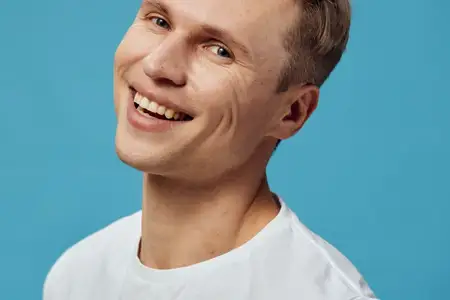 Улыбающийся счастливый молодой мужчина европеоидной расы в белой рубашке смотрит в камеру на изолированном синем фоне с положительными эмоциями и расслабленным настроением