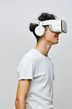 Молодой человек, полностью поглощенный опытом виртуальной реальности, в VR-гарнитуре и наушниках на фоне мягкого светло-серого фона, который подчеркивает современные технологии и эффект погружения