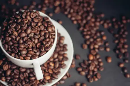 Чашка с кофейными зернами стоит на блюдце на сером фоне, крупный план