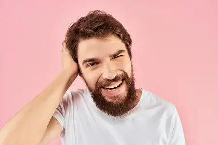 Крупный план бородатого мужчины в белой футболке, который жестикулирует руками и выражает эмоции на лице