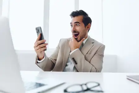Привлекательный мужчина в деловом костюме сидит в офисе с ноутбуком и телефоном