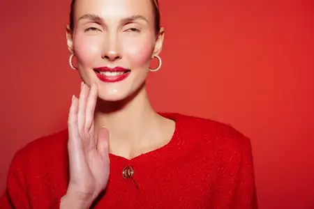 Счастливая женщина в красном свитере и серьгах-кольцах машет рукой